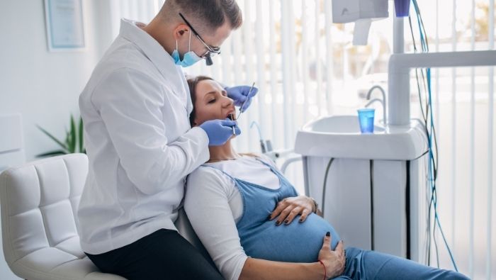 Dentista atendendo uma gestante reclinada na cadeira odontológica durante exame.