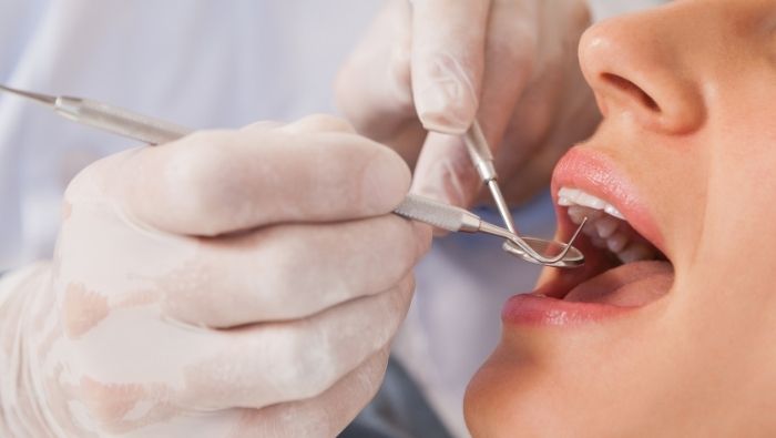 Dentista examinando a boca de uma paciente com instrumentos odontológicos e luvas.